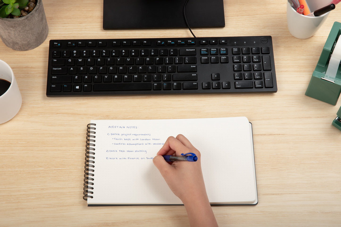 Person taking notes in using a Plana Flex on a desk with a keyboard and office supplies.